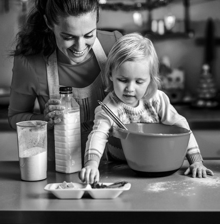 Baby helping mother make christmas cookies in christmas decorated kitchenの写真素材