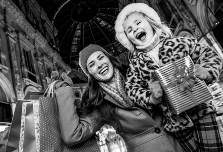 On a huge Christmas sales in Italian fashion capital. happy young mother and daughter tourists in Galleria Vittorio Emanuele II in Milan, Italy with Christmas present box and shopping bags rejoicingの写真素材