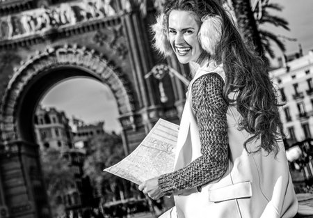 in Barcelona for a perfect winter. happy modern woman in earmuffs near Arc de Triomf in Barcelona, Spain with mapの写真素材