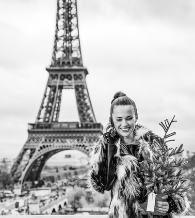 The Party Season in Paris. smiling modern fashion-monger with Christmas tree in fur coat against Eiffel tower in Paris, France talking on a mobile phoneの写真素材