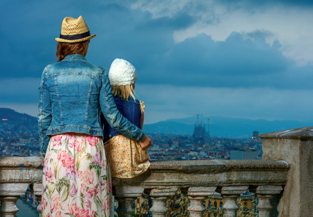 Perfect evening with stunning view. Seen from behind elegant mother and daughter travellers against city panorama of Barcelona, Spain looking into the distanceの写真素材