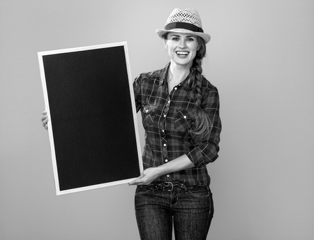 Healthy food to your table. Portrait of smiling young woman grower in checkered shirt isolated on yellow showing blank boardの写真素材