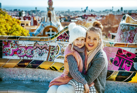 Barcelona signature style. Portrait of smiling modern mother and daughter tourists at Guell Park in Barcelona, Spain hugging while sitting on a benchの写真素材