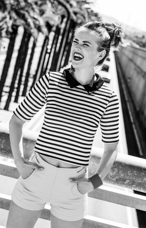 Nosing around, having fun. smiling trendy woman in yellow shorts and stripy shirt against highway in the city looking into the distanceの写真素材