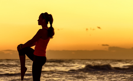 Refreshing wild sea side workout. Silhouette. Full length portrait of active woman in sport clothes on the seashore stretchingの写真素材