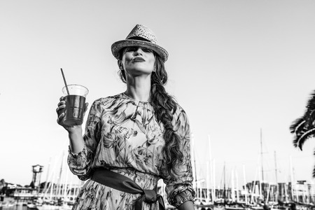 Summertime at colorful Barcelona. trendy tourist woman in long dress and straw hat in Barcelona, Spain with bright red beverage having fun timeの写真素材