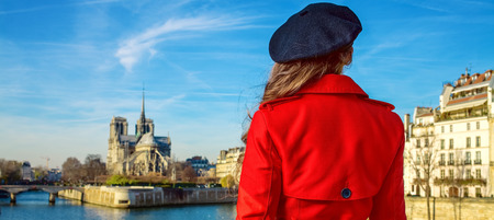 Seen from behind trendy woman in red trench coat on embankment near Notre Dame de Paris in Paris, Franceの写真素材