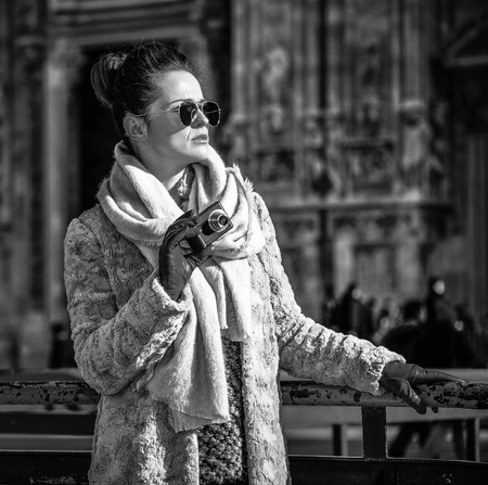 Rediscovering things everybody love in Milan. trendy tourist woman in fur coat and sunglasses in the front of Cathedral in Milan, Italy looking into the distance while holding digital photo cameraの写真素材