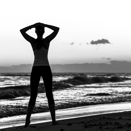 Refreshing wild sea side workout. Silhouette. Full length portrait of relaxed young woman in sports gear standing on the seacoastの写真素材