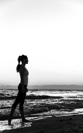 Refreshing wild sea side workout. Silhouette. Full length portrait of healthy woman in sportswear on the beach walkingの写真素材