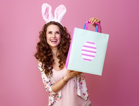 Festive bunny and eggs season. happy modern woman in Easter bunny ears isolated on pink background with Easter shopping bag looking at copy spaceの写真素材
