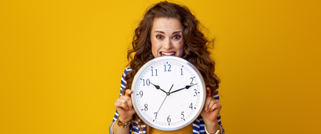 stressed trendy woman in striped jacket on yellow background biting clockの写真素材