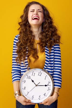 sad stylish woman with long wavy brunette hair isolated on yellow background with clockの写真素材