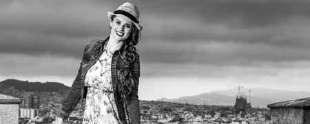 Perfect evening with stunning view. happy elegant traveller woman in long dress and straw hat against cityscape of Barcelona, Spainの写真素材
