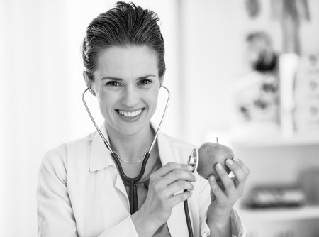 Happy medical doctor woman examining apple with stethoscopeの写真素材