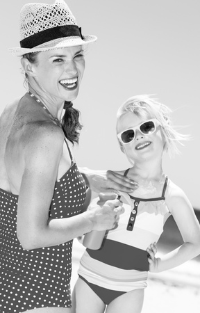 sea, white sand paradise. smiling young mother and daughter in swimwear on the beach applying suntan lotionの写真素材