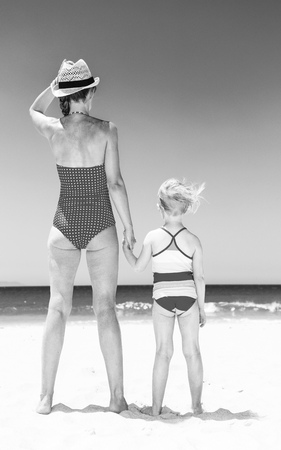sea, white sand paradise. Seen from behind young mother and child in beachwear on the seashore looking into the distanceの写真素材