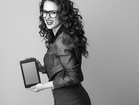 smiling trendy woman with long wavy brunette hair showing tablet PC blank screen against backgroundの写真素材