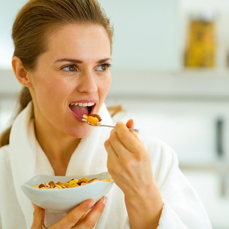 Young housewife in bathrobe having healthy breakfast in kitchenの写真素材