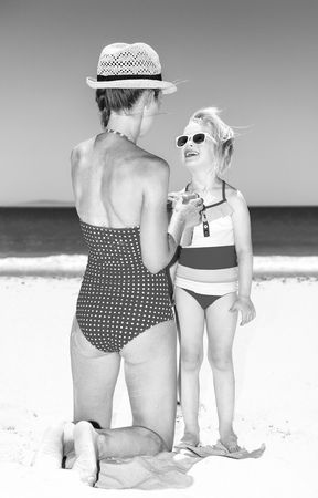 sea, white sand paradise. happy modern mother and child in swimsuit on the beach applying sun screenの写真素材