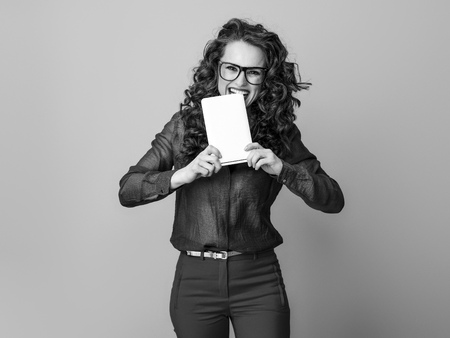 Portrait of smiling trendy woman with long wavy brunette hair biting tablet PC isolated on backgroundの写真素材