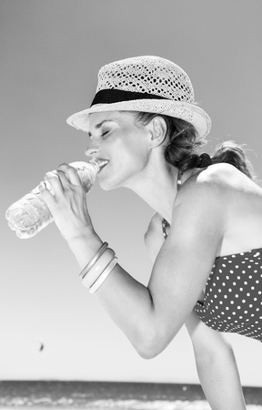 sea, white sand paradise. Portrait of smiling young woman in beachwear on the beach drinking water from bottleの写真素材