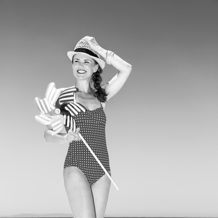 sea, white sand paradise. smiling young woman in bright swimwear on the seashore with windmill toy looking into the distanceの写真素材