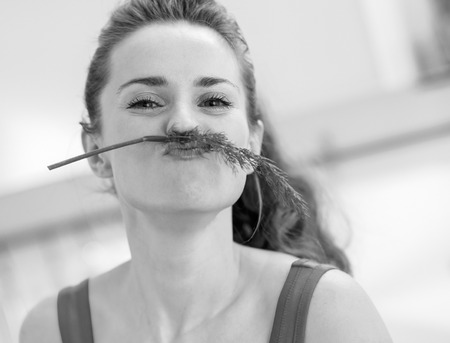 Funny young woman using dill as mustache in kitchenの写真素材