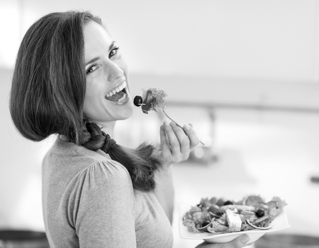 Smiling young woman eating fresh salad in modern kitchenの写真素材