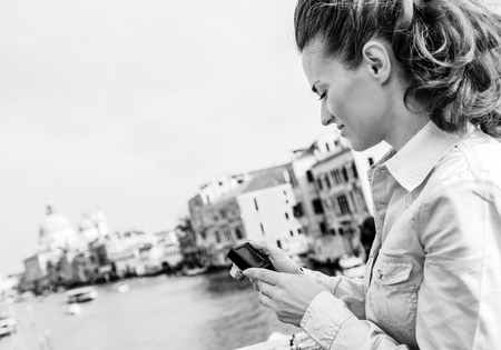 Young woman standing on bridge with grand canal view in venice, italy and checking photos in cameraの写真素材