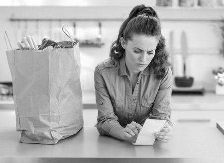 Concerned housewife checking bill after shopping in kitchen