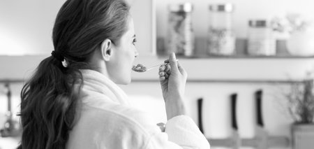 Young woman in bathrobe eating breakfast. rear view