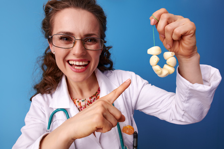 smiling paediatrist woman in white medical robe pointing at garlic beads isolated on blueの写真素材