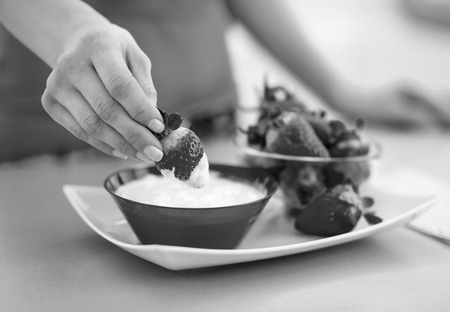Closeup on happy young woman eating strawberry with yogurt in kitchenの写真素材