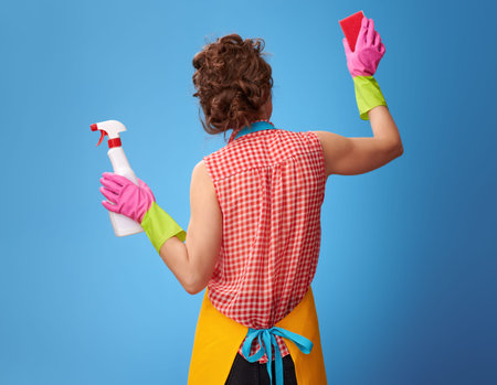 Big cleaning time. Seen from behind young woman in a yellow apron with cleaning detergent using...