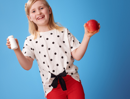 smiling modern girl in red pants with an apple and bottles of vitamins on blue backgroundの写真素材