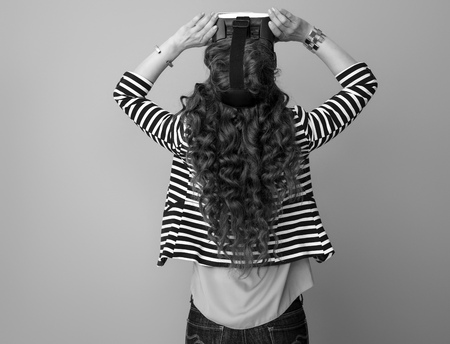 Seen from behind modern woman with long wavy brunette hair against background in VR glassesの写真素材