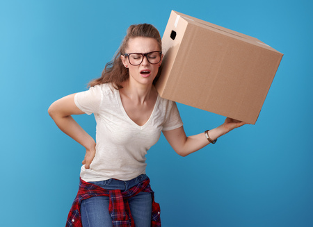 modern woman in white shirt with a cardboard box having backache isolated on blue backgroundの写真素材