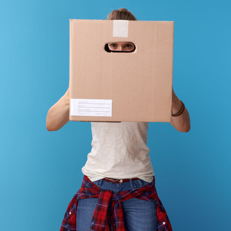 active hipster in white shirt looking through a cardboard box isolated on blue