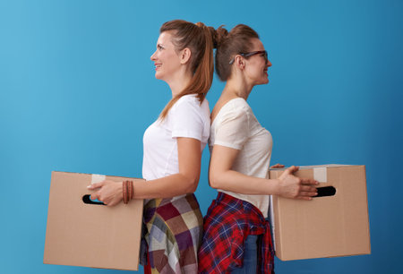 smiling modern hipster roommates in white shirts with a cardboard boxes standing back to back...