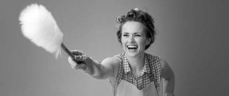 Big cleaning time. happy modern woman in a apron using a duster brush against backgroundの写真素材