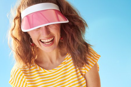 happy healthy woman in yellow shirt against blue sky hiding behind sun visorの写真素材