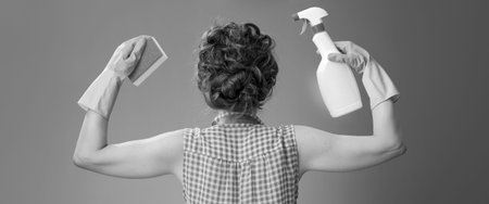 Big cleaning time. Seen from behind modern woman in a apron with kitchen sponge and a bottle of detergent showing biceps isolated onの写真素材