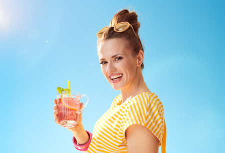 happy fit woman in yellow shirt against blue sky with refreshing cocktailの写真素材