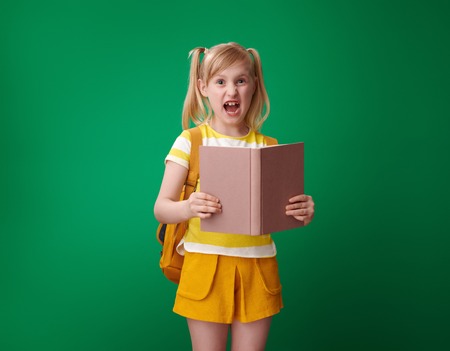 annoyed school girl with backpack with an open book on green backgroundの写真素材