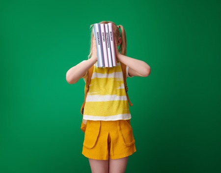 pupil with backpack holding schoolbooks in the front of face against green backgroundの写真素材