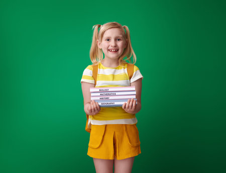 happy pupil with backpack with schoolbooks isolated on green