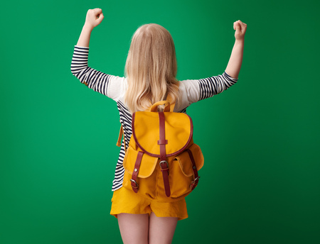 Seen from behind pupil with backpack rejoicing against green backgroundの写真素材
