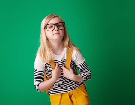 tired school girl with backpack on green backgroundの写真素材
