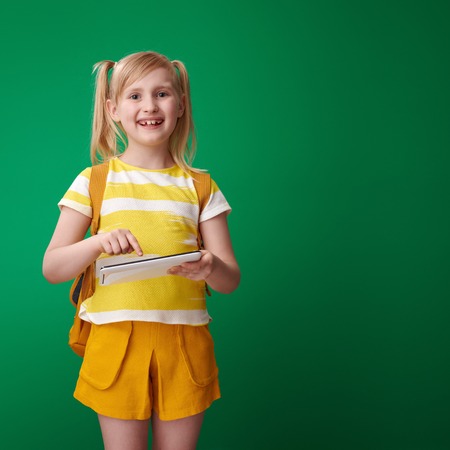happy pupil with backpack using tablet PC isolated on green backgroundの写真素材